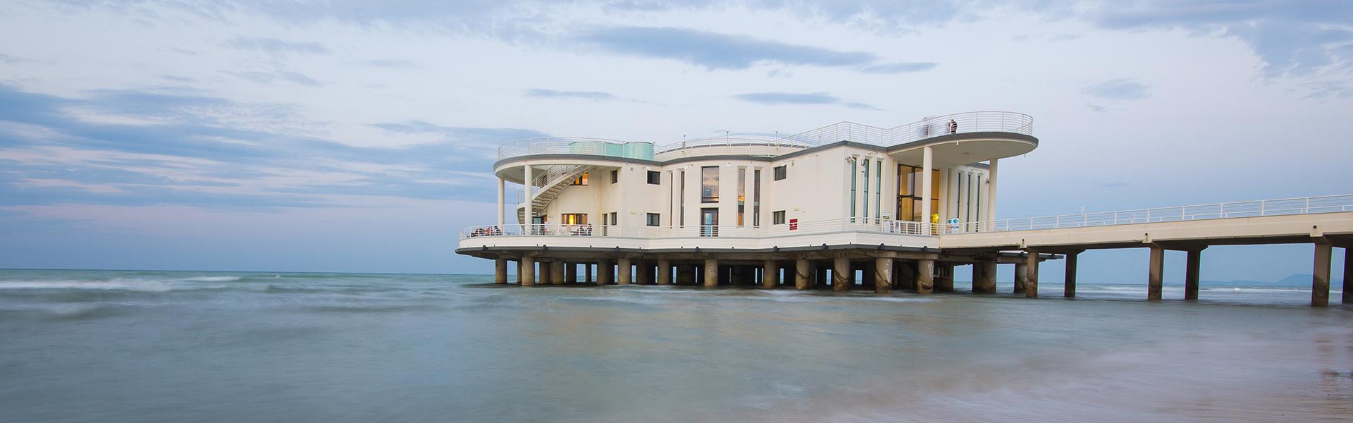Edificio moderno su palafitte in riva al mare, cielo nuvoloso.