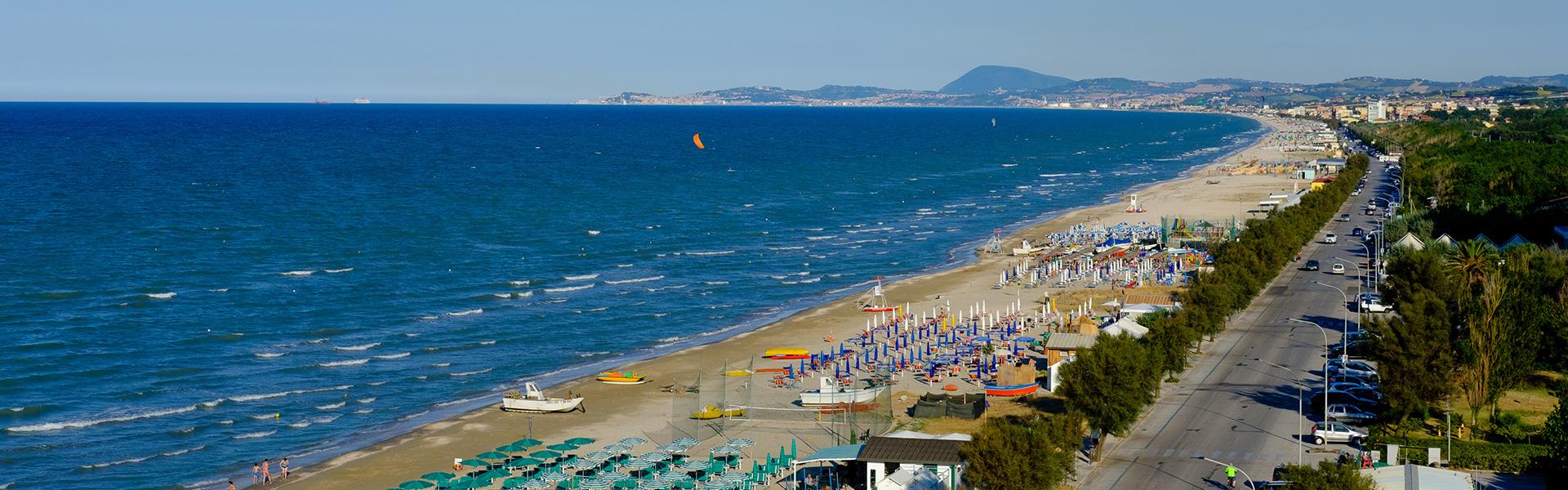 Spiaggia affollata con ombrelloni colorati lungo la costa adriatica, vista panoramica.