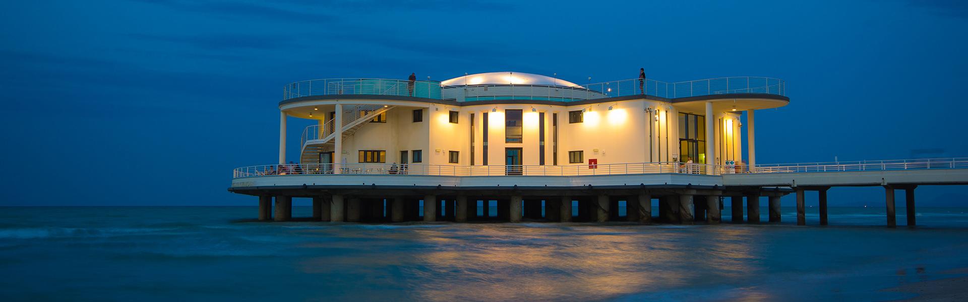 Edificio sul mare al tramonto con spiaggia sabbiosa e onde leggere.